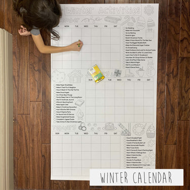 A large printable coloring banner titled 'WINTER CALENDAR' laid out on the floor with a child coloring on it, with various winter activities listed for each day.
